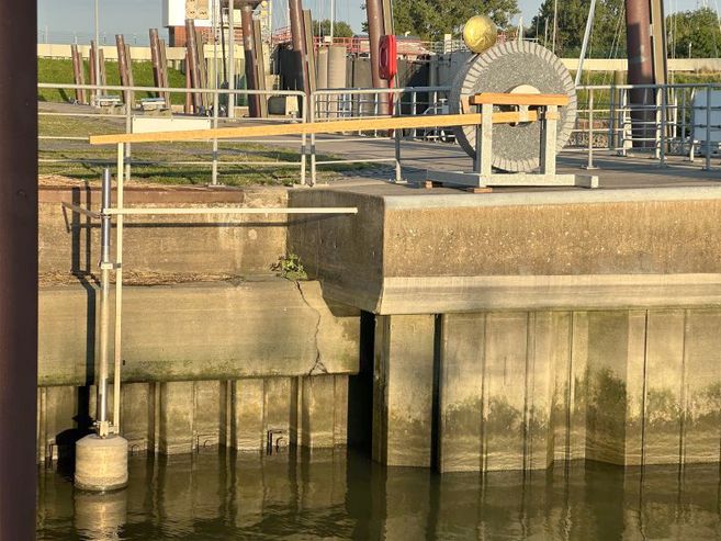Ein Schwimmer an einer Betonmauer in einem Hafenbereich mit Geländer und mechanischer Vorrichtung im Hintergrund.