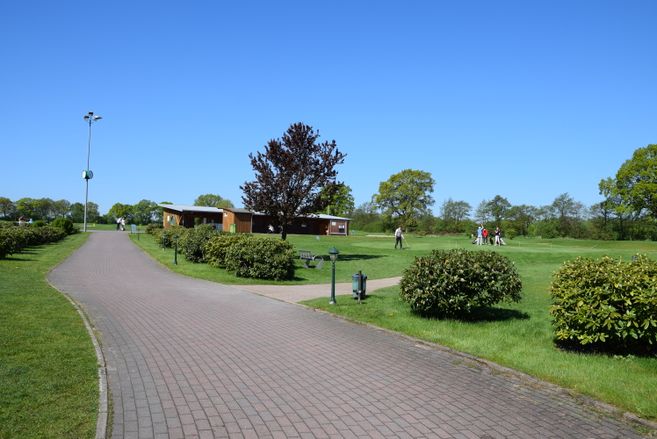 Golfplatz mit Übungsbereich und Personen beim Golfspielen unter blauem Himmel.