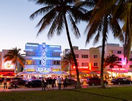 Das Bild zeigt den Ocean Drive in Southbeach Miami im Abendlicht mit leuchtenden Neon-Schildern. 